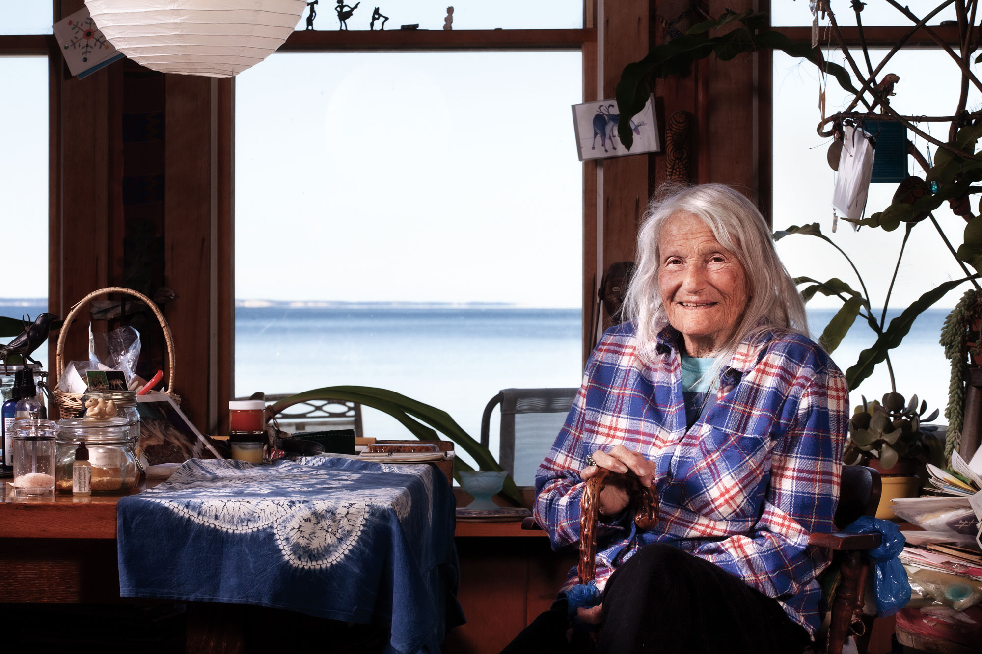 Provincetown painter Pat de Groot seated in her home with a view of the ocean through windows behind her